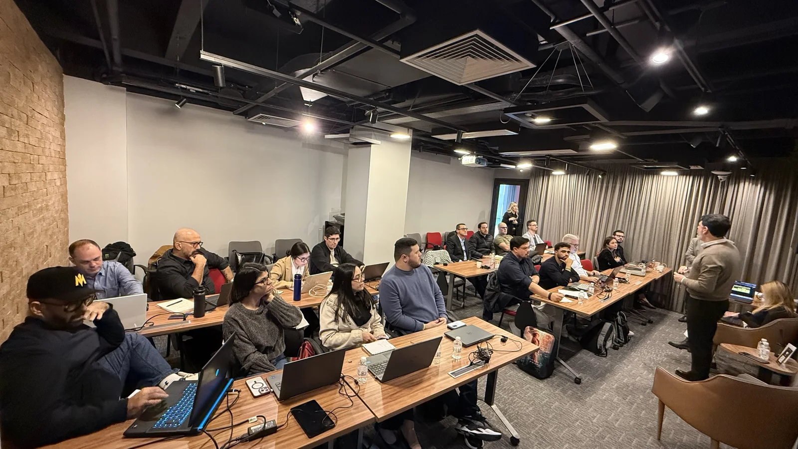Empresários com notebooks abertos nas mesas de um encontro presencial da Brave